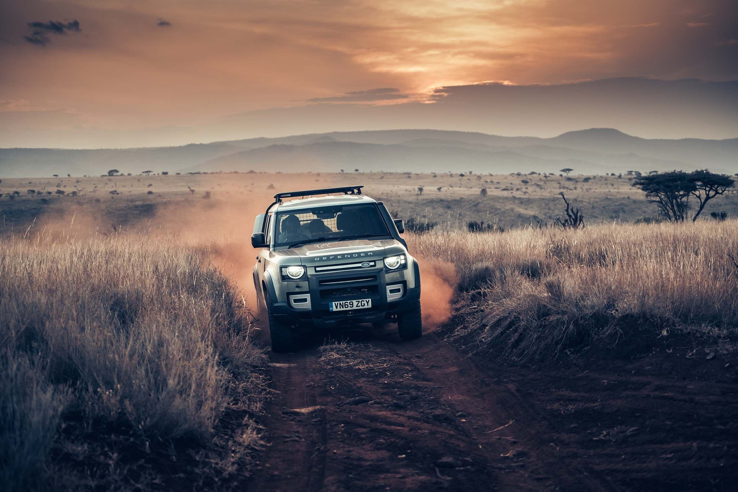 a land rover defender is driving down a dirt road in the desert .