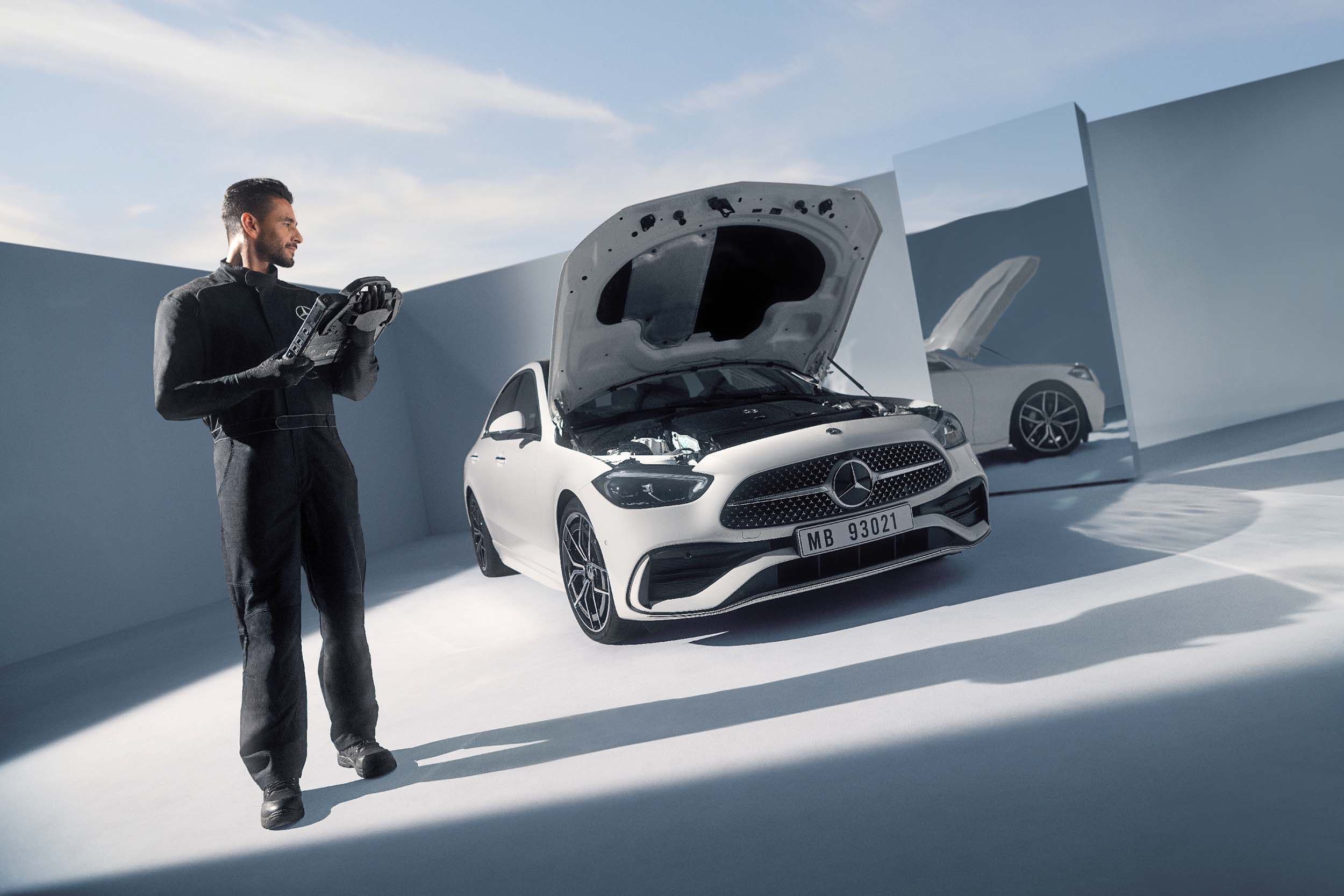a man is standing next to a white mercedes with the hood open .
