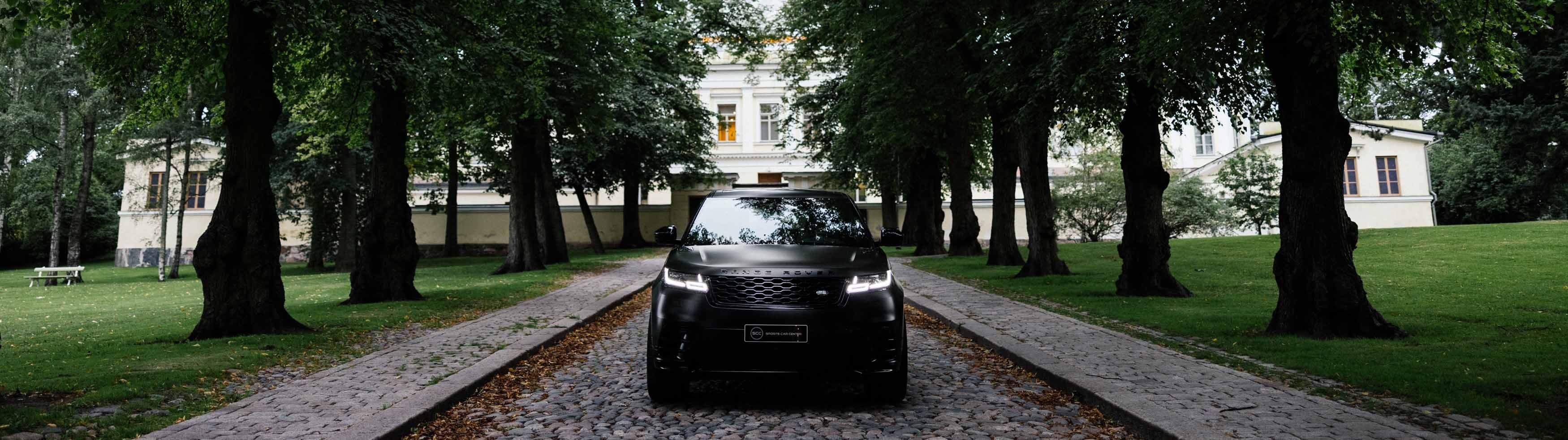 a black range rover is parked on a cobblestone driveway surrounded by trees .