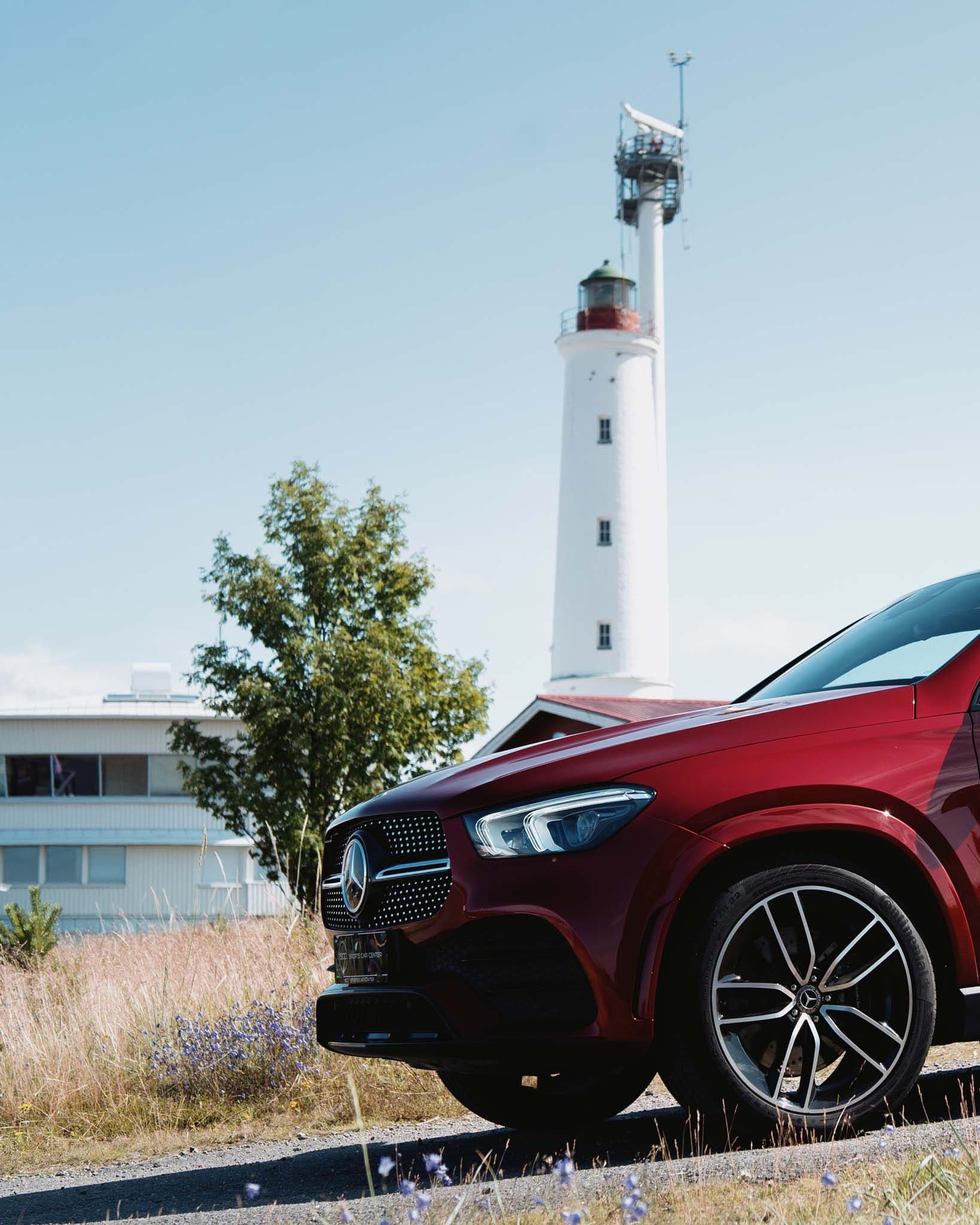 a red mercedes benz is parked on the side of the road in front of a lighthouse .